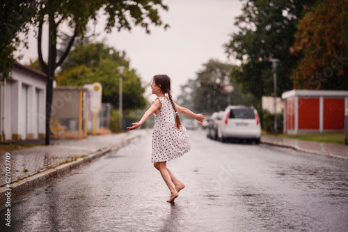 Little preschooler girl in white dress with black hearts dancing and spinning on wet empty street under the rain © Иванна Емельянова