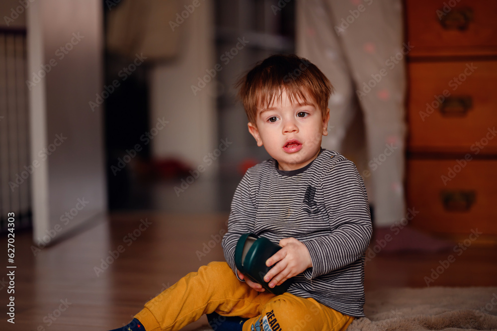 Fototapeta premium Little thoughtful toddler boy sitting on floor playing with glasses case