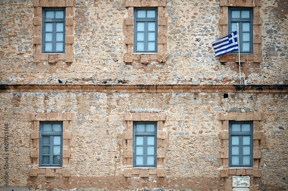 Fototapeta premium an old stone building with a Greek flag, Syntagma Square, Nafplio
