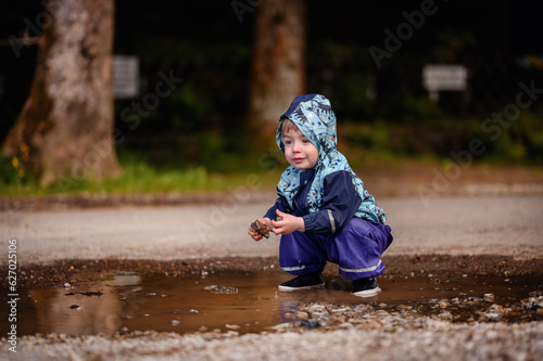 Fototapeta Naklejka Na Ścianę i Meble -  Little toddler boy in waterproof wearing playing in puddle with water