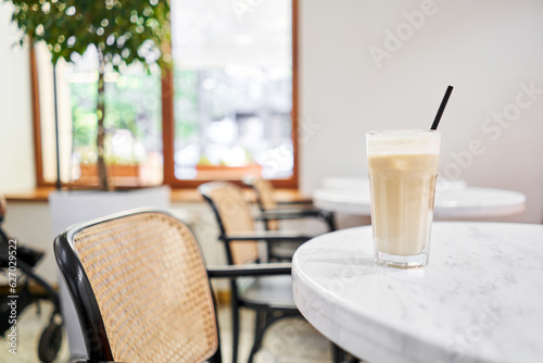 Glass of cold cappuccino with ice. The table in the coworking space of the coffee shop. A cup of coffee on the veranda on a sunny day. Coffee break at the cafe. Close-up