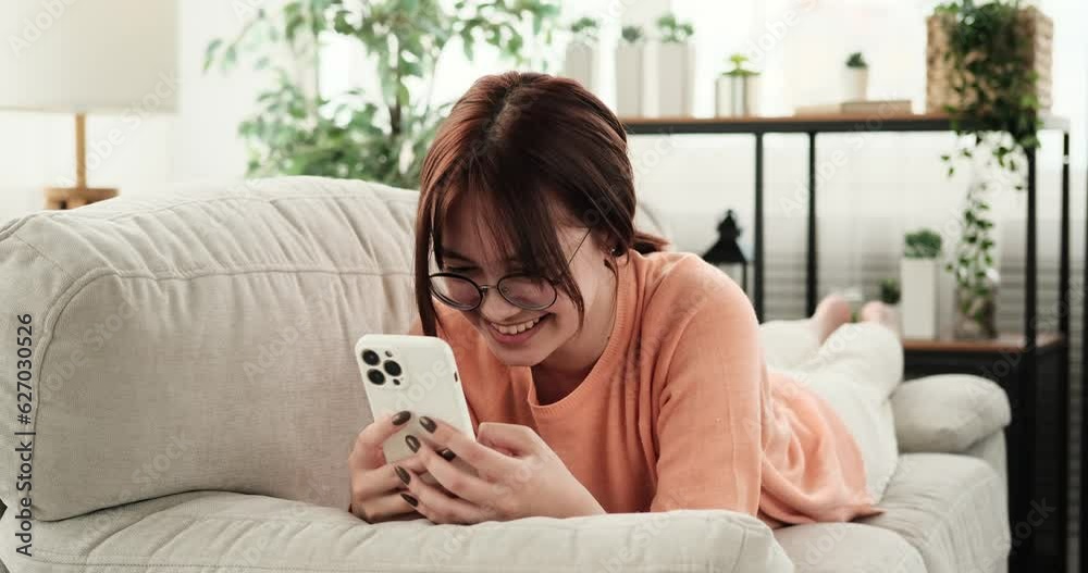 While lying on the couch, a caucasian teenage girl receives a message on her phone, and face instantly lights up with a joyful smile. She reads the message, and a burst of laughter escapes her lips.