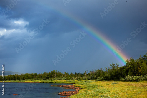 Rainbow by the side of the Lainio river in the Swedish Lapland with dramatic dark sky and clouds in the background on summer afternoon. photo