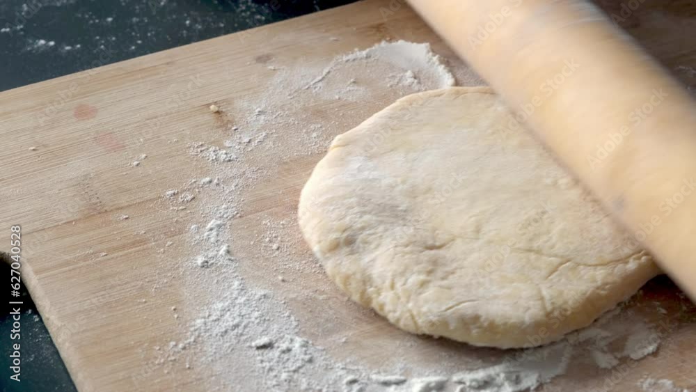 rolls out the dough for baking bread with a rolling pin on a wooden board close-up of a far-fetched kitchen rolls out the dough for baking bread with a rolling pin on a wooden board close-up of a far-fetched kitchen