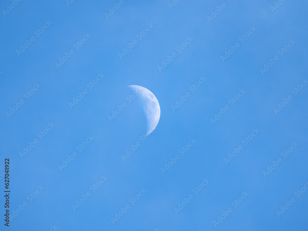 Half moon during daylight. Moon is in the blue sky. Half moon during daylight. Moon is in the blue sky.