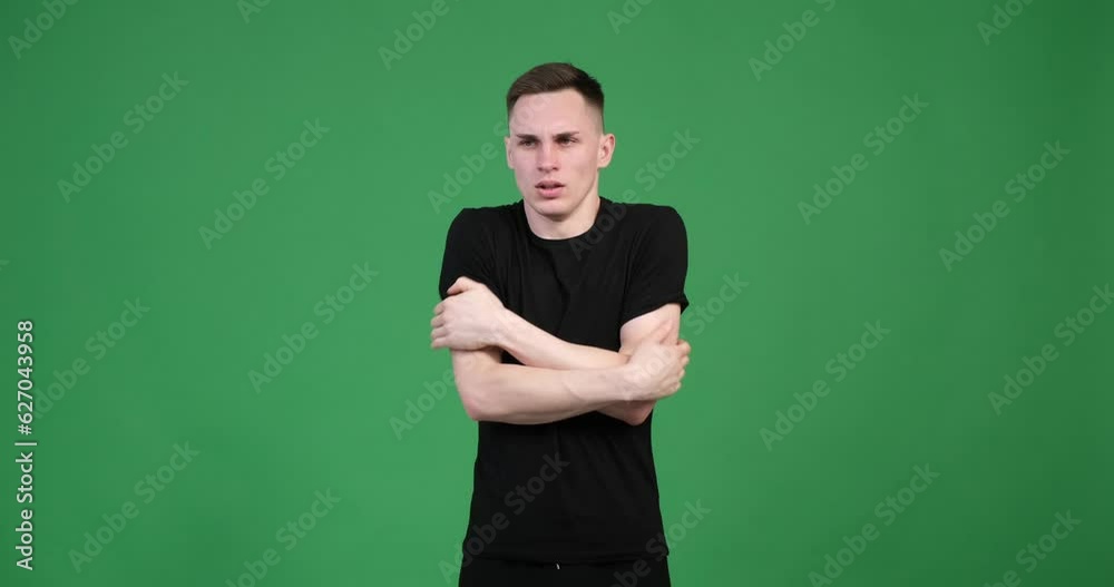 An unhappy man is seen shivering and stretching his arms on a green screen backdrop. His face displays a clear expression of discontent, reflecting the discomfort caused by the cold. An unhappy man is seen shivering and stretching his arms on a green screen backdrop. His face displays a clear expression of discontent, reflecting the discomfort caused by the cold.