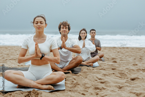The beachside lotus. Young people meditating together during yoga lesson outdoors, sitting on mats on the beach © Prostock-studio
