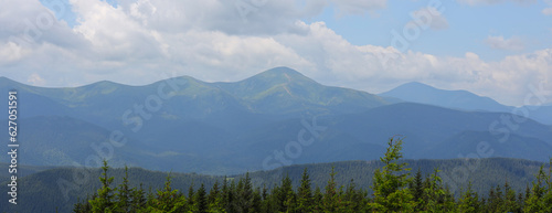 Mountain range with green trees and the peaks are visible. The sky is blue with white clouds. © Andrii Zastrozhnov