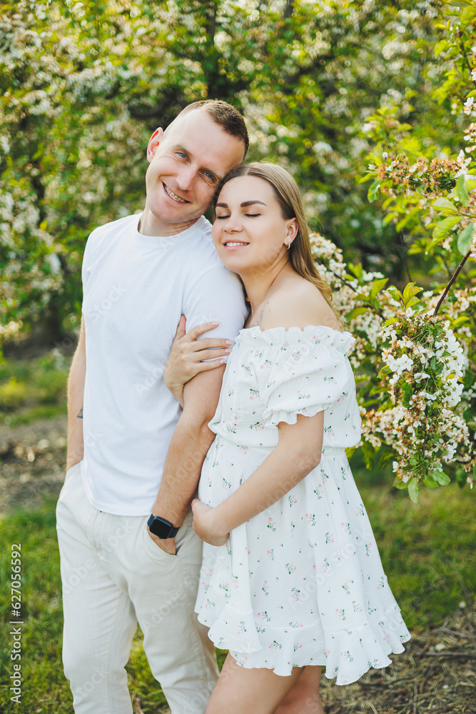 Beautiful young couple in spring garden. Beauty lifestyle family concept. A happy mother is expecting a baby. A happy young couple in a blooming garden Beautiful young couple in spring garden. Beauty lifestyle family concept. A happy mother is expecting a baby. A happy young couple in a blooming garden