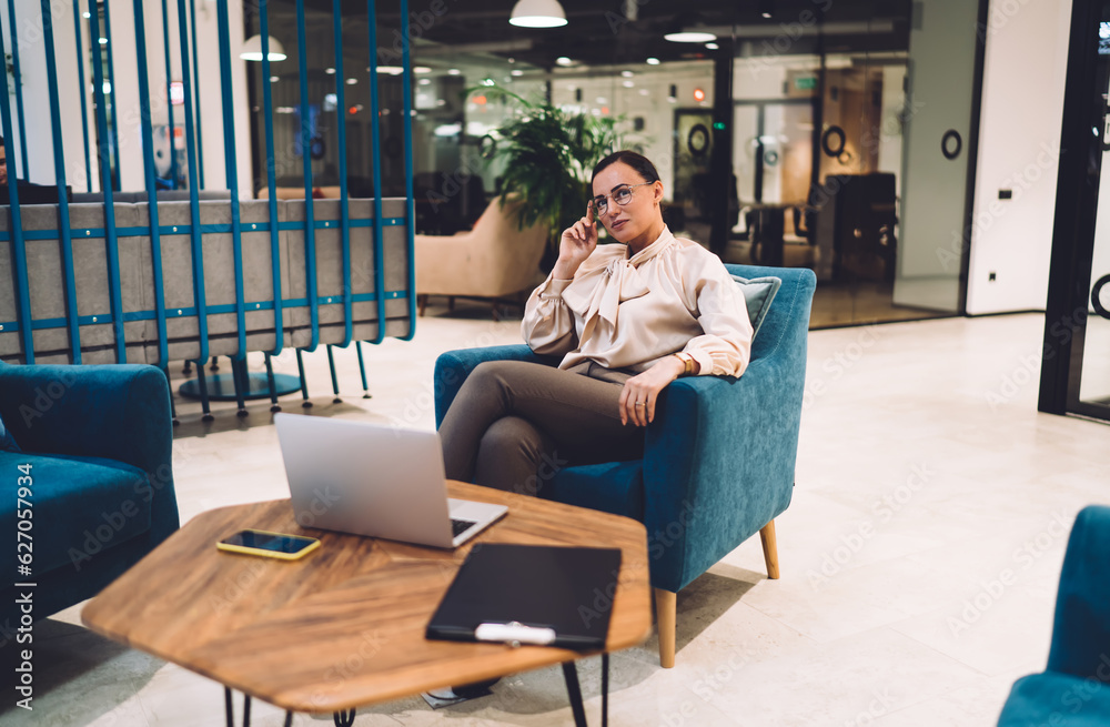 Fototapeta premium Positive female executive in glasses resting on armchair after work on laptop
