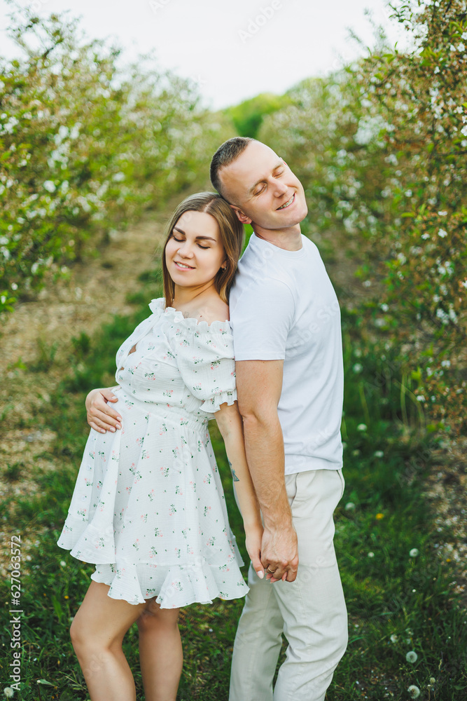 Beautiful young couple man and pregnant woman in spring garden. Beauty lifestyle family concept. A happy mother is expecting a baby. A happy young couple in a blooming garden
