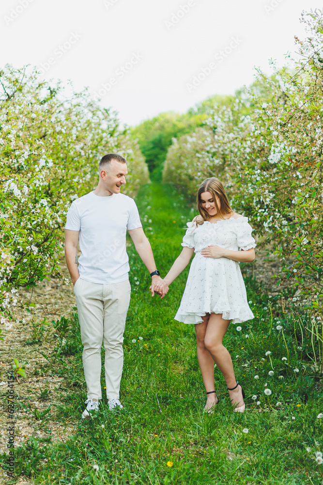 Beautiful young couple in spring garden. Beauty lifestyle family concept. A happy mother is expecting a baby. A happy young couple in a blooming garden Beautiful young couple in spring garden. Beauty lifestyle family concept. A happy mother is expecting a baby. A happy young couple in a blooming garden