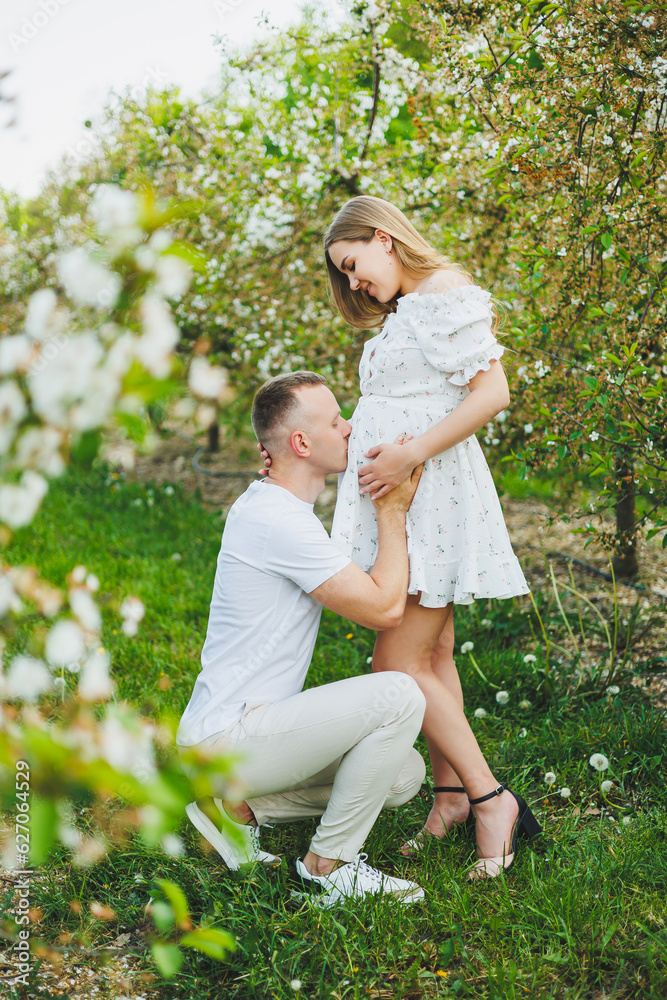 Fototapeta premium Beautiful young couple in spring garden. Beauty lifestyle family concept. A happy mother is expecting a baby. A happy young couple in a blooming garden
