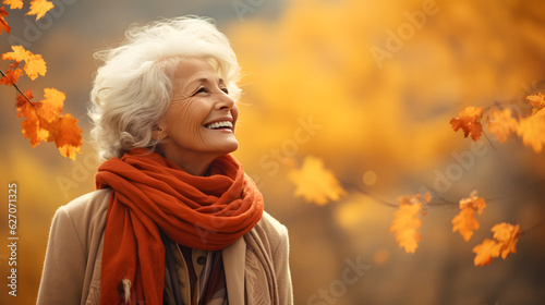Portrait of an elderly happy smiling woman in autumn park, positive cheerful aged lady enjoying a walk outdoors in autumn forest