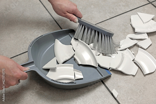 dustpan and brush used to clean a broken plate from the kitchen floor.