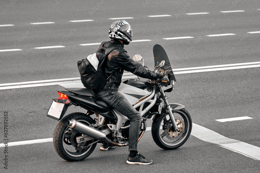 A man on a black and white road bike stands at a traffic light. A motorcyclist in a leather jacket is ready to start the journey. Biker made a stop on the road. A man on a black and white road bike stands at a traffic light. A motorcyclist in a leather jacket is ready to start the journey. Biker made a stop on the road.