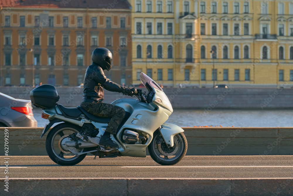 A motorcyclist in a helmet rides along the river on a green sports touring motorcycle. A man travels on a motorbike through a beautiful city.