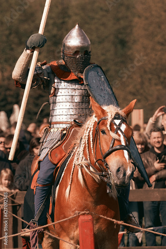 A medieval knight with a spear and shield on horseback prepares for a duel in front of the audience. Reconstruction of a jousting tournament in our time, a show for modern people.