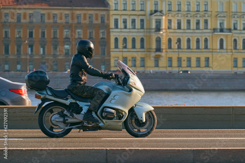 A motorcyclist in a helmet rides along the river on a green sports touring motorcycle. A man travels on a motorbike through a beautiful city.