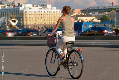 Fototapeta Naklejka Na Ścianę i Meble -  A young female cyclist rides a bicycle next to a city road clogged with cars. Beautiful slender childfree girl enjoys riding a bike.