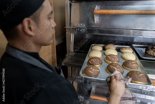 Un joven panadero Hispano sacando conchas mexicanas del horno photo