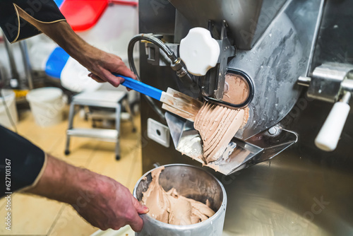 Ice making concept. Indoors closeup shot of professional worker using ice cream maker and gathering product in steel container. Ice cream machine being used in kitchen. High quality photo