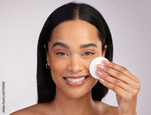 Happy woman, portrait and cotton pad in skincare or makeup removal against a grey studio background. Face of female person wiping product, cosmetics or remove with swab in cleanse or facial treatment