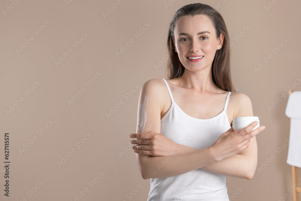 Happy woman applying body cream onto arm on beige background, space for text Happy woman applying body cream onto arm on beige background, space for text