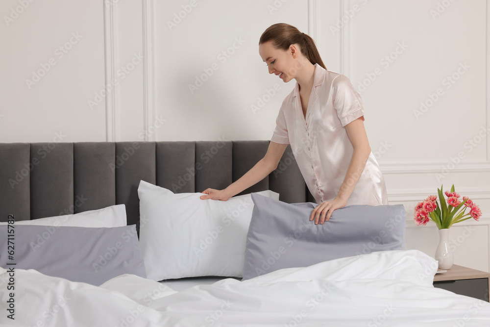 Young beautiful woman making bed in room Young beautiful woman making bed in room