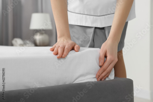 Young maid making bed in hotel room, closeup