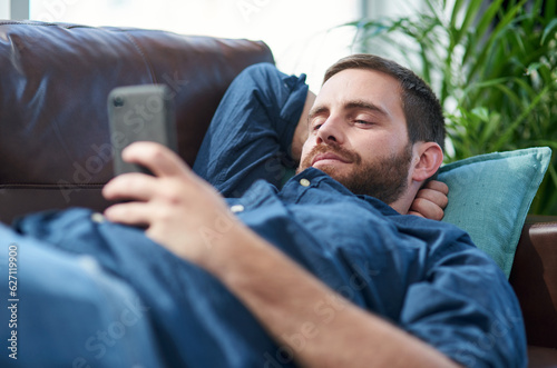 Recharge and bounce back better than ever. Shot of a young man using a smartphone while relaxing on a sofa.