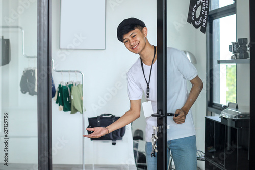 Young attractive Asian retail fashion shop owner at store opening the door for customer
