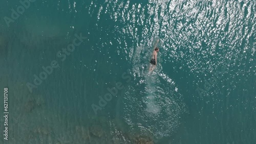 Aerial drone view of man swimming in glacier alpine lake, exploring the Swiss Alps on a sunny day
