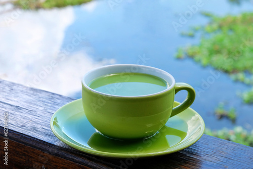 a cup of milk green tea on the table beside lake. the addition of milk to green tea may help mitigate the potential bitterness or astringency of some green teas, making it more enjoyable.