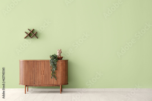 Modern chest of drawers with houseplant near green wall in room