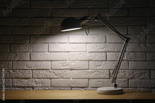 Glowing lamp on wooden table near white brick wall in dark room