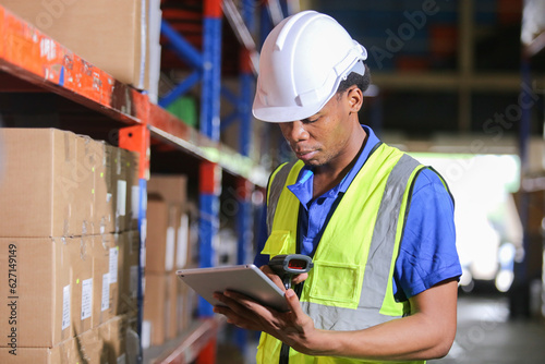 Man american african professional worker wearing safety uniform and hard hat using digital tablet inspect product on shelves in warehouse. Man worker check stock inspecting in storage logistic.