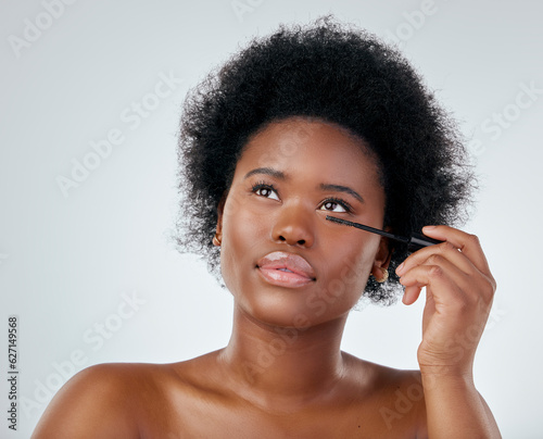Black woman, makeup and brush for mascara or beauty with afro against a white background in studio. Face of African person or model applying eye product, cosmetics or lashes for facial treatment
