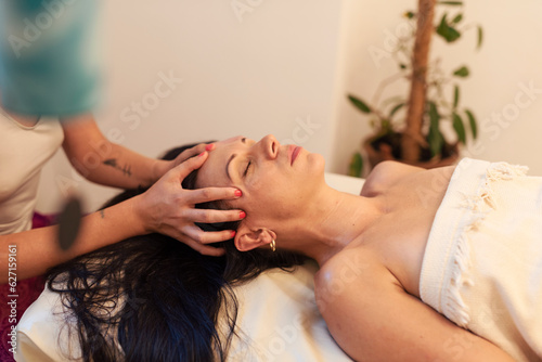 Wellness, beauty and relaxation concept. Beautiful young woman lying with closed eyes and having face and head massage at spa. Welness and therapy with specialist.