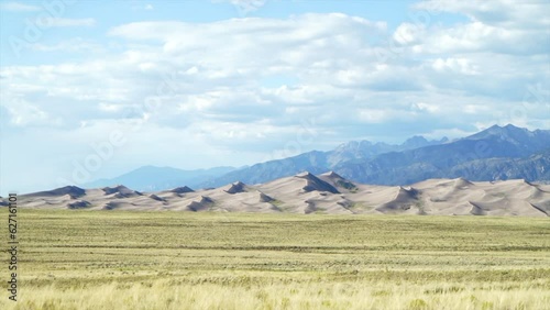 Stunning late summer early fall view of The Great Sand Dunes National Park Colorado Rockies mountain sandy 14er peaks crisp golden yellow tall grass wind clouds blue sky mid day cinematic car motion photo