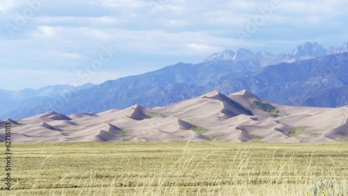 Stunning late summer early fall view of The Great Sand Dunes National Park Colorado Rockies mountain sandy 14er peaks crisp golden yellow tall grass wind clouds blue sky mid day cinematic slow motion photo