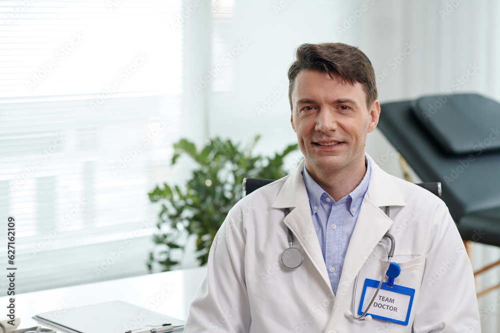 Portrait of smiling plastic surgeon in white labcoat standing in office of clinic Portrait of smiling plastic surgeon in white labcoat standing in office of clinic