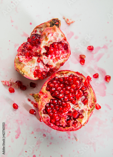 Smashed opened juicy pomegranate fruit on white background. Food photography with fresh and juicy pomegranate with red arils or seeds.