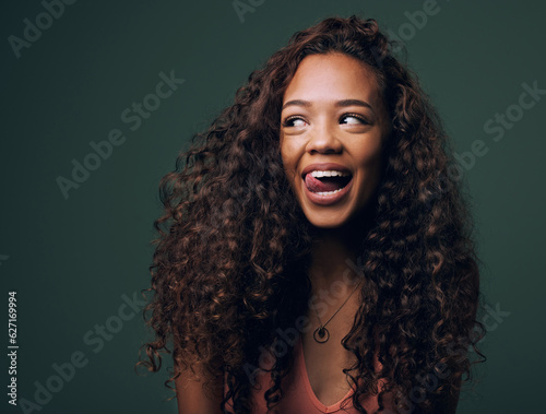 Natural beauty, tongue out and happy gen z girl with hair, curly and curious on green background. Afro, wellness care and female model with fun, emoji and silly face, personality or comic in studio