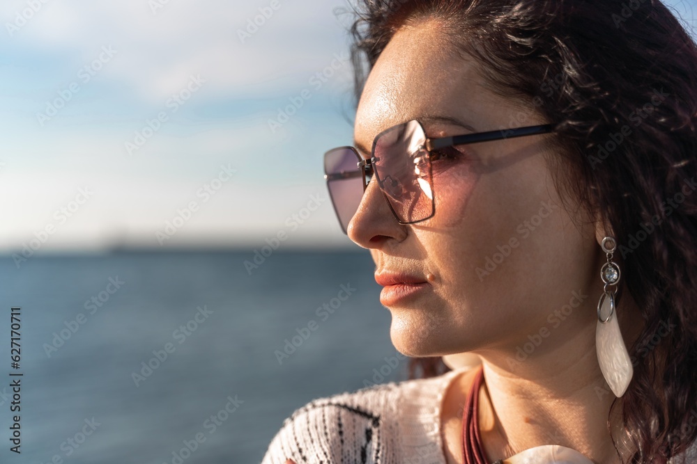 Portrait of a curly woman in glasses on the background of the sea. Vacation on the sea, walk, tourism. Portrait of a curly woman in glasses on the background of the sea. Vacation on the sea, walk, tourism.
