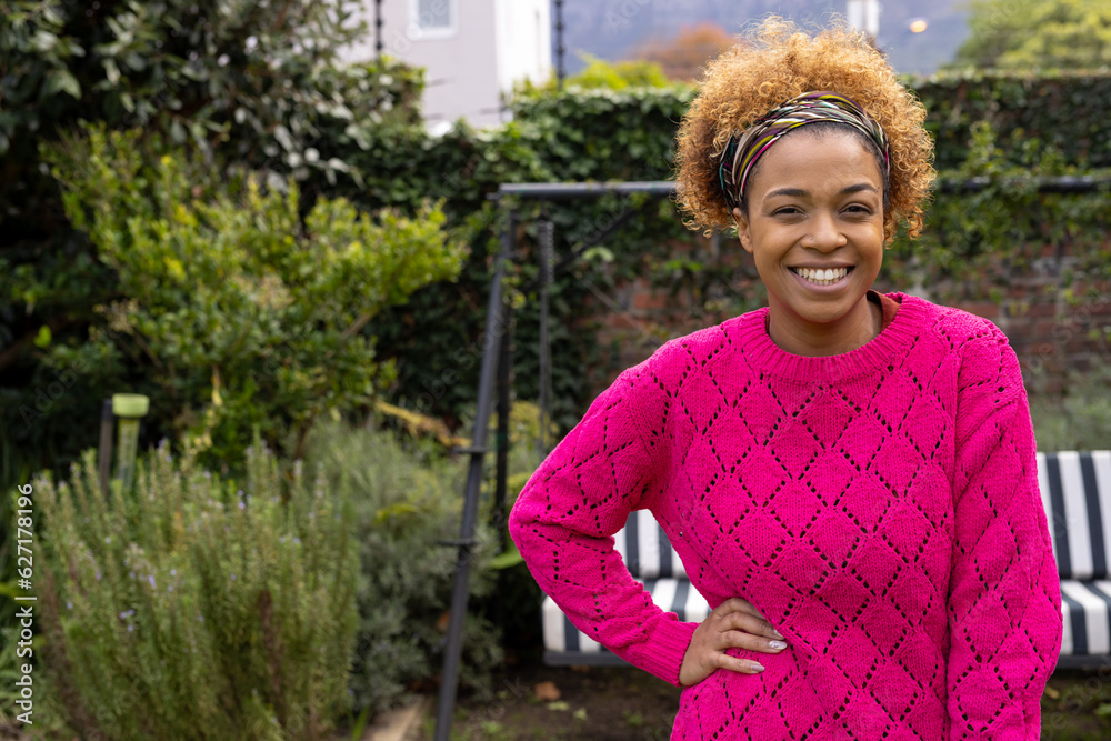 Portrait of happy african american woman wearing pink sweater, smiling in garden, copy space