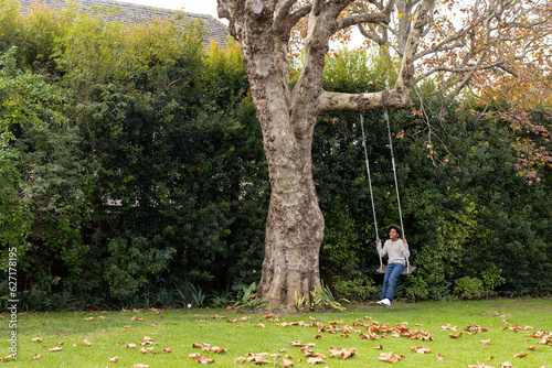 Happy african american boy swinging on tree swing in garden, copy space photo