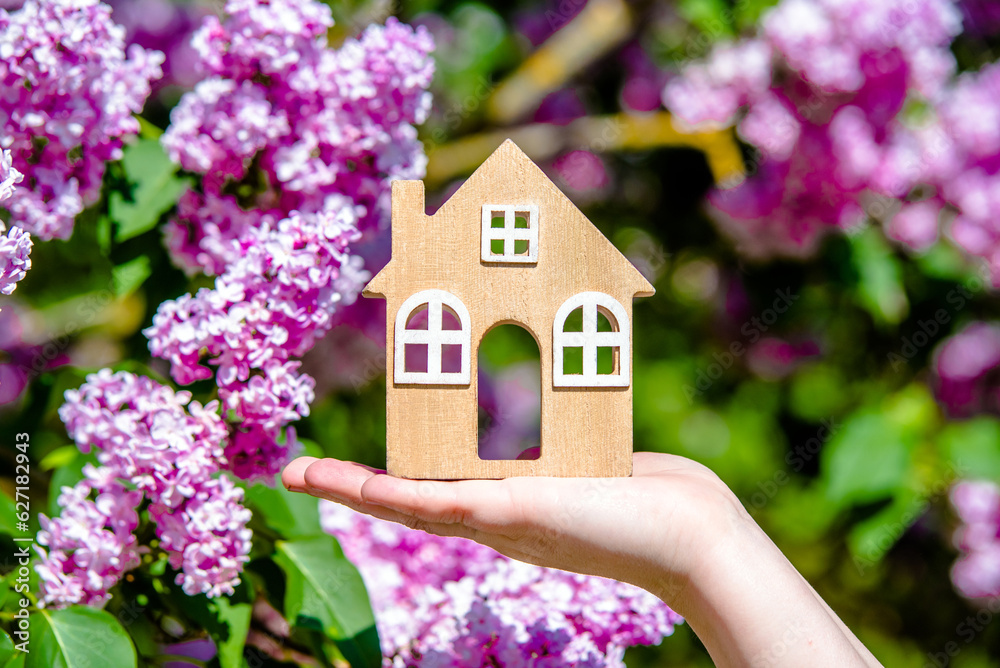 The girl holds in her hand the symbol of the house against the background of blooming lilac
The girl holds in her hand the symbol of the house against the background of blooming lilac