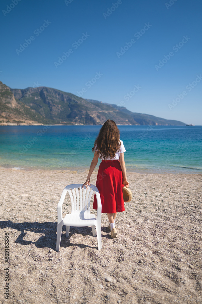 A girl in a red skirt on an empty beach near a chair