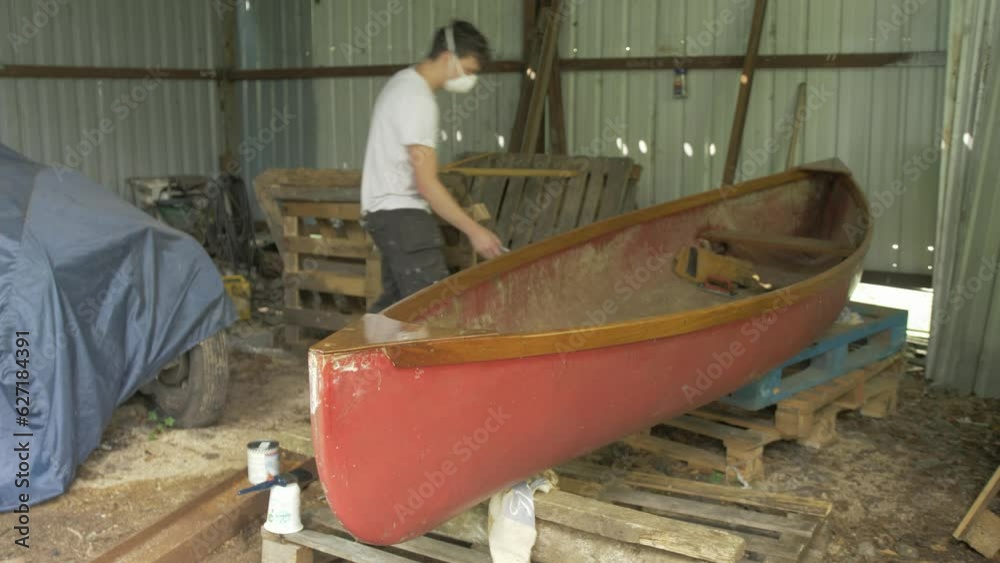 A young male carpenter cleans up after repairing a canoe A young male carpenter cleans up after repairing a canoe